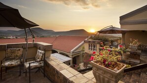 Une terrasse offrant une vue sur les montagnes et un magnifique coucher de soleil, avec des sièges d’extérieur et des plantes en pot.