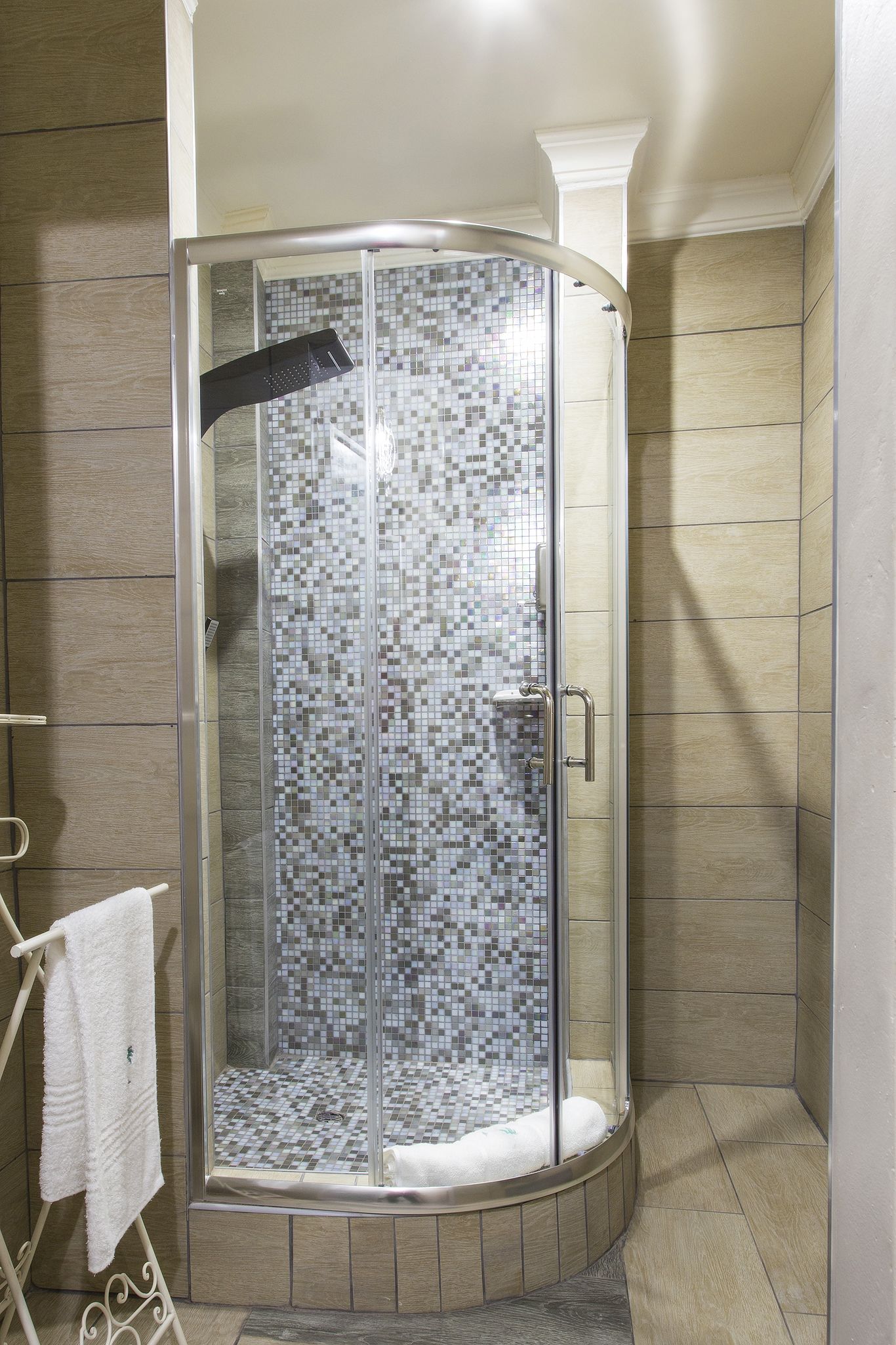 Une douche d’angle avec une porte en verre et un revêtement mural intérieur en mosaïque.