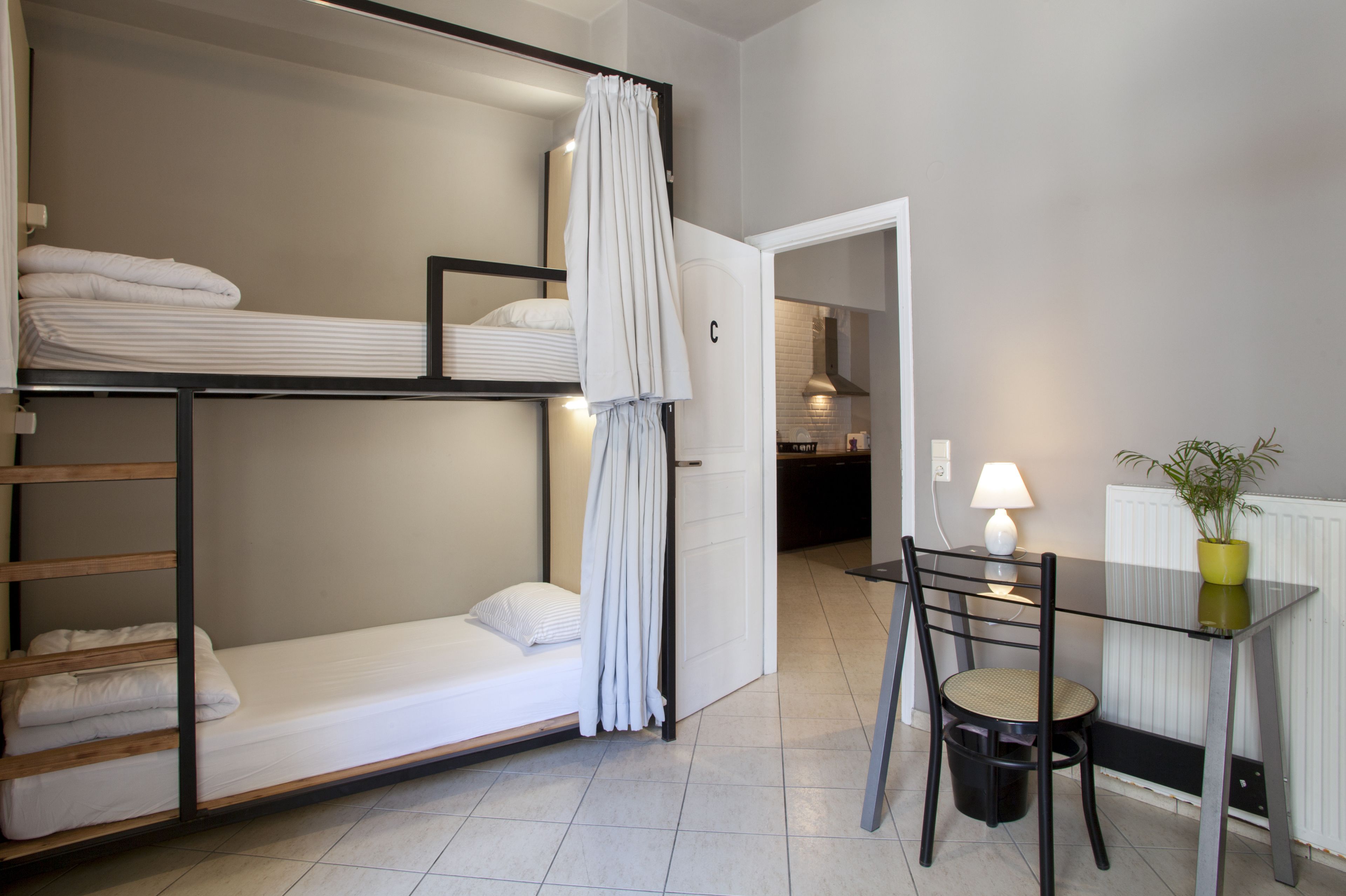 A bunk bed with white bedding, a table with a chair, a lamp, and a potted plant.