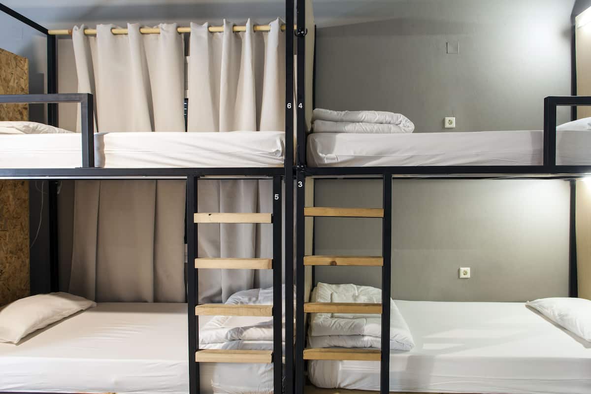 Ein Mehrbettzimmer mit Stockbetten, einer Leiter, Vorhängen und einer neutralen Farbgestaltung.