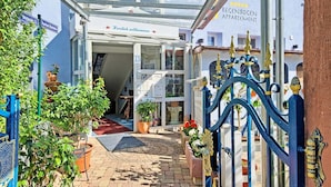 A hotel entrance with a glass canopy, a blue gate, and potted plants. - Regenbogen Appartement (Bad Krozingen)