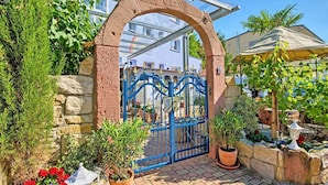 A brick archway leading to a courtyard with a blue gate, potted plants, and outdoor seating. - Regenbogen Appartement (Bad Krozingen)