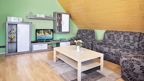 A living room with a green wall, a wooden ceiling, a sofa, a TV, a cabinet, and a coffee table. - Regenbogen Appartement (Bad Krozingen)
