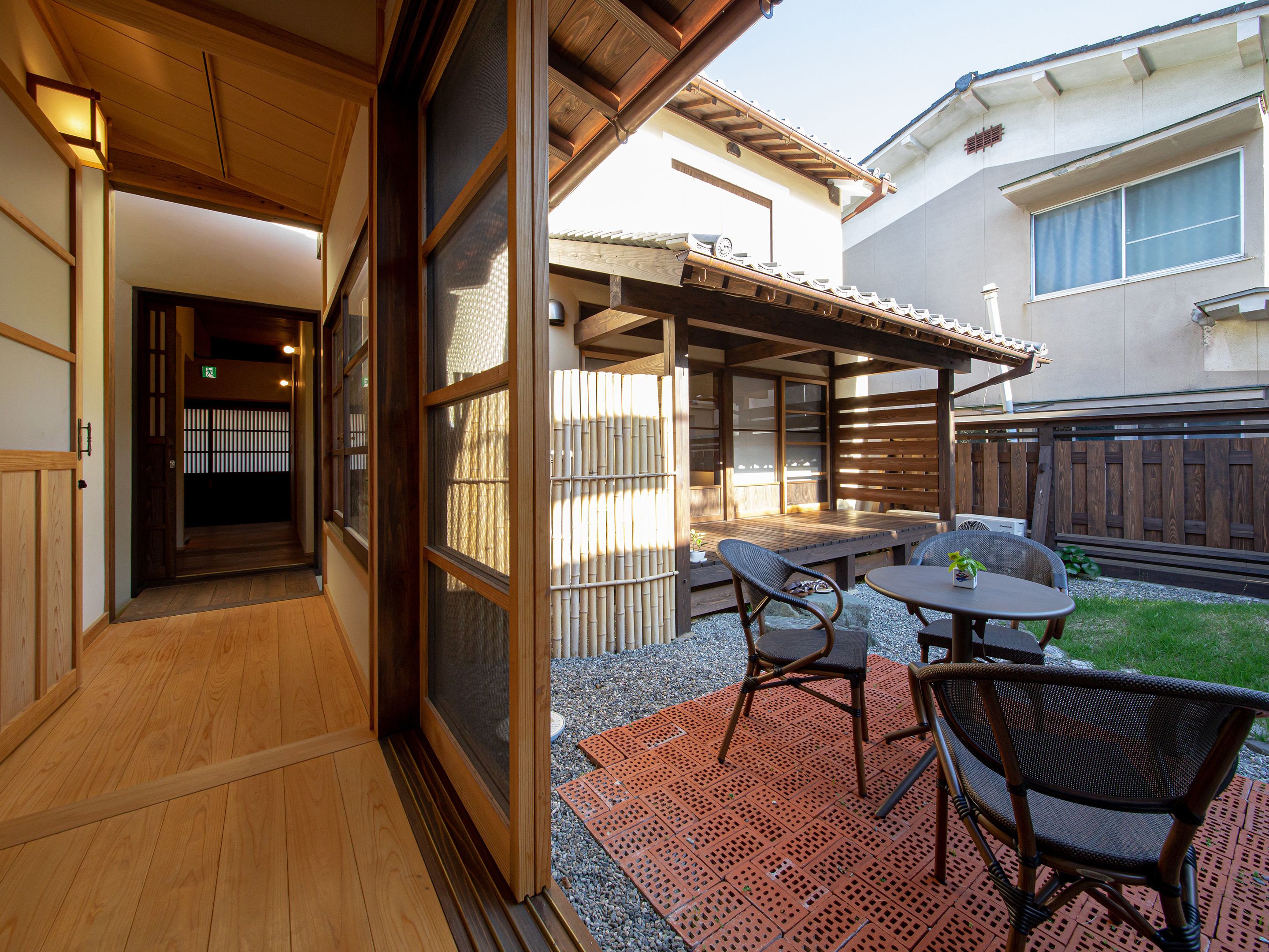 A traditional Japanese-style outdoor patio with tatami flooring, a wooden table, and two wicker chairs.
