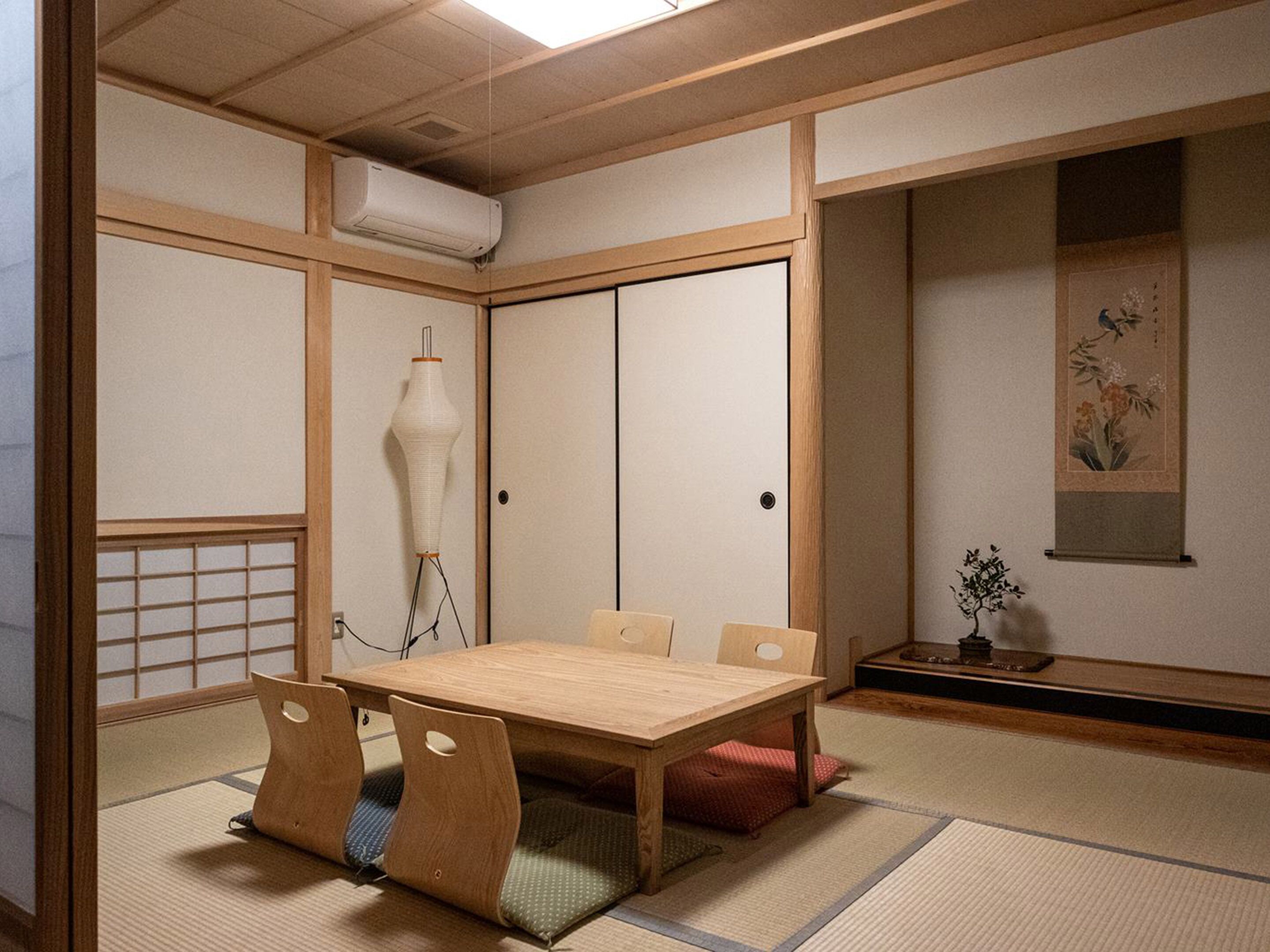 A traditional Japanese-style room with tatami flooring, a wooden table with cushions, a shoji screen door, and a hanging lamp.
