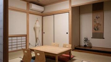 A traditional Japanese-style room with tatami flooring, a wooden table with cushions, a shoji screen door, and a hanging lamp.