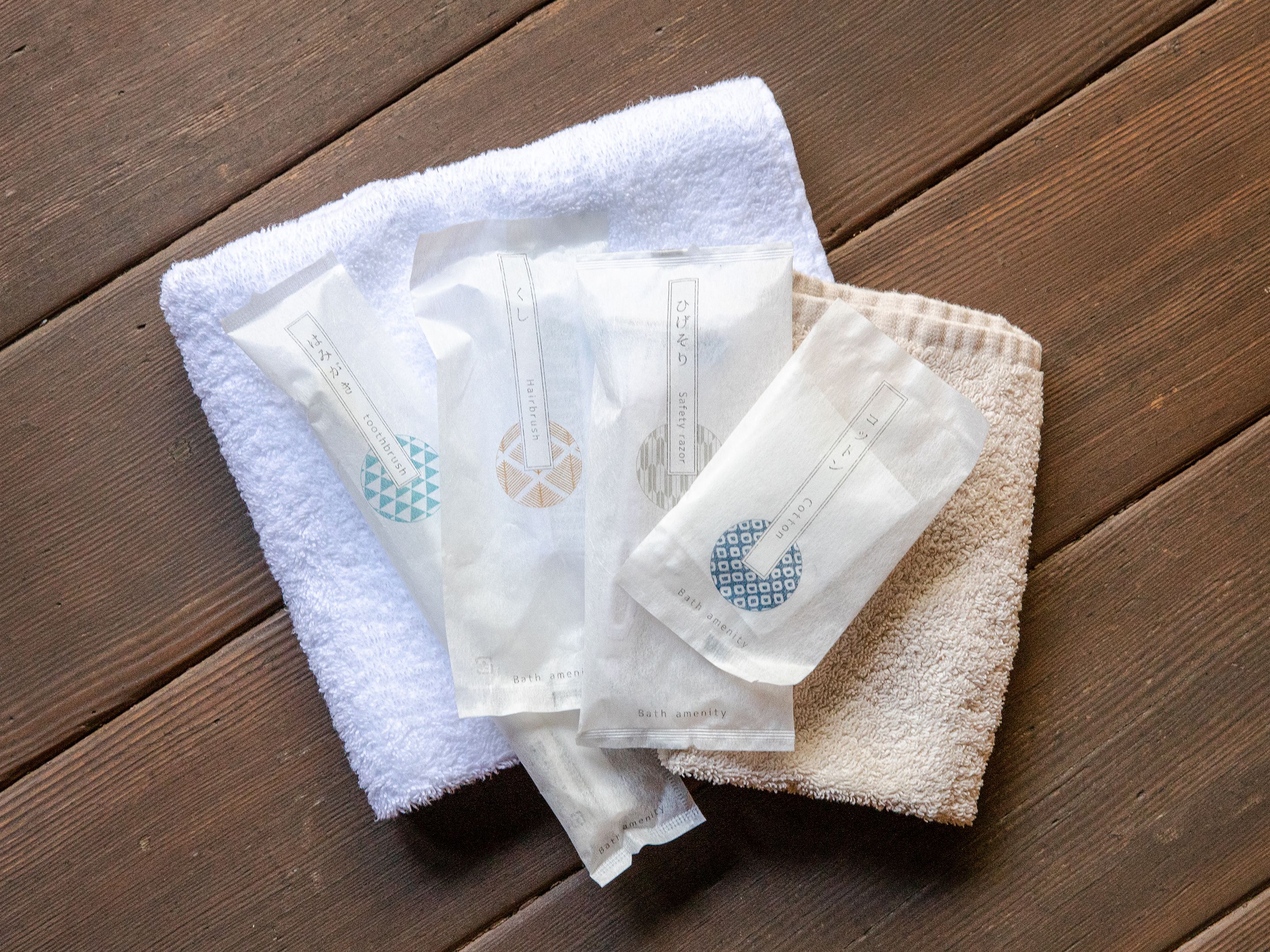 A wooden surface with a white towel and three small white packets labeled with different amenities.