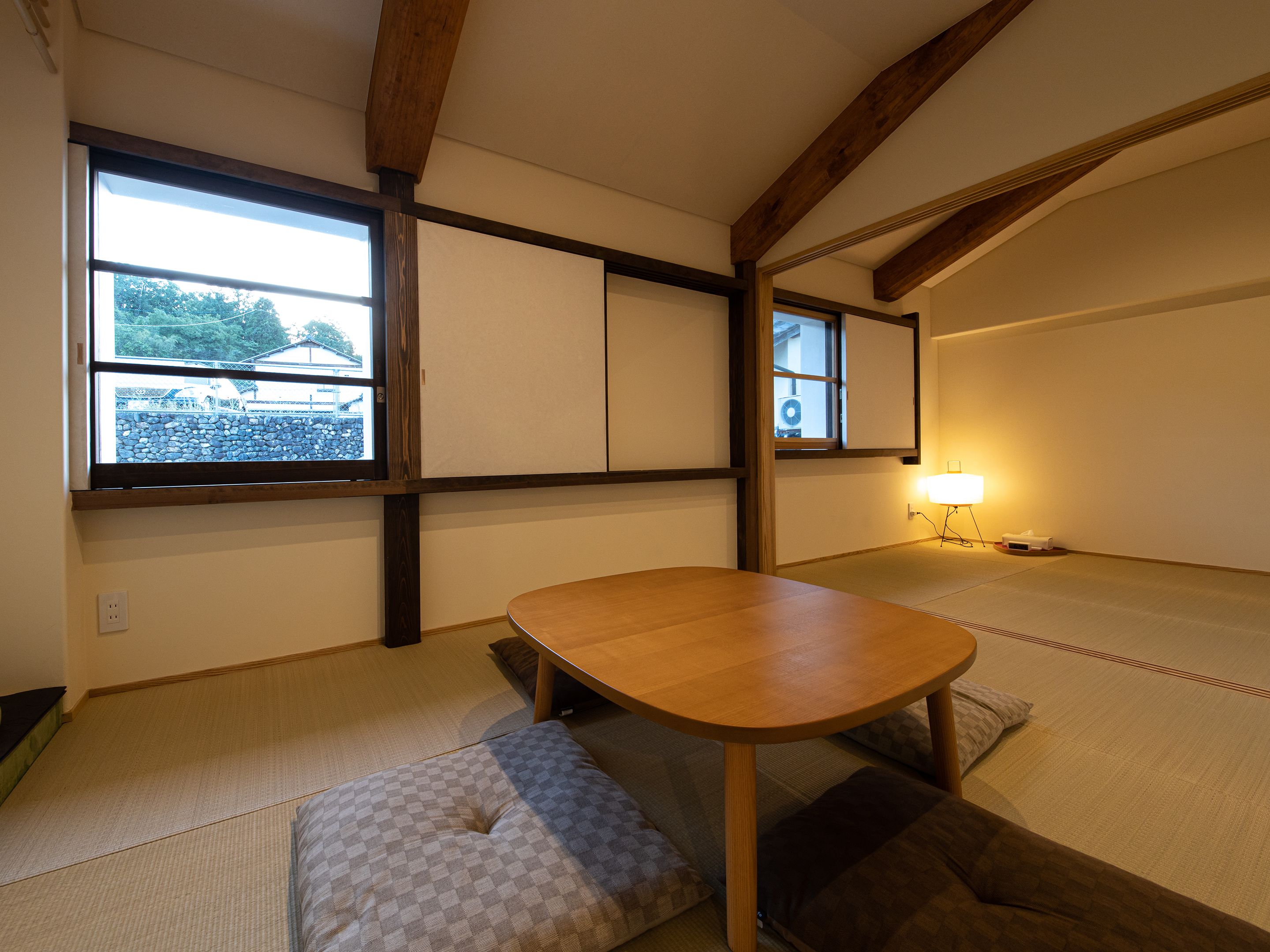 A traditional Japanese room with tatami flooring, a low wooden table, and a view of a parking lot through a large window.