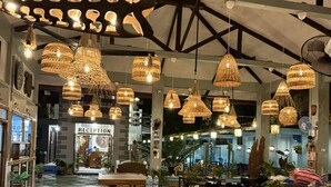 A restaurant with hanging wicker chandeliers, stone tile flooring, and a reception area in the background. - Ferellee Beachfront Inn (San Vicente)