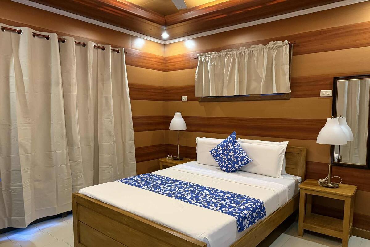 A wooden-paneled room with a bed, two bedside lamps, and a window with curtains.