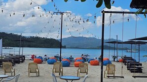 A beachside café with outdoor seating, tables, and chairs, overlooking a calm sea and distant mountains. - Ferellee Beachfront Inn (San Vicente)