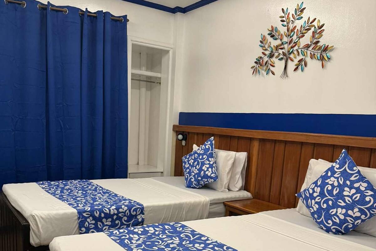 A hotel room with two beds, each with a blue and white patterned bedspread, a wooden headboard, and a decorative wall piece.
