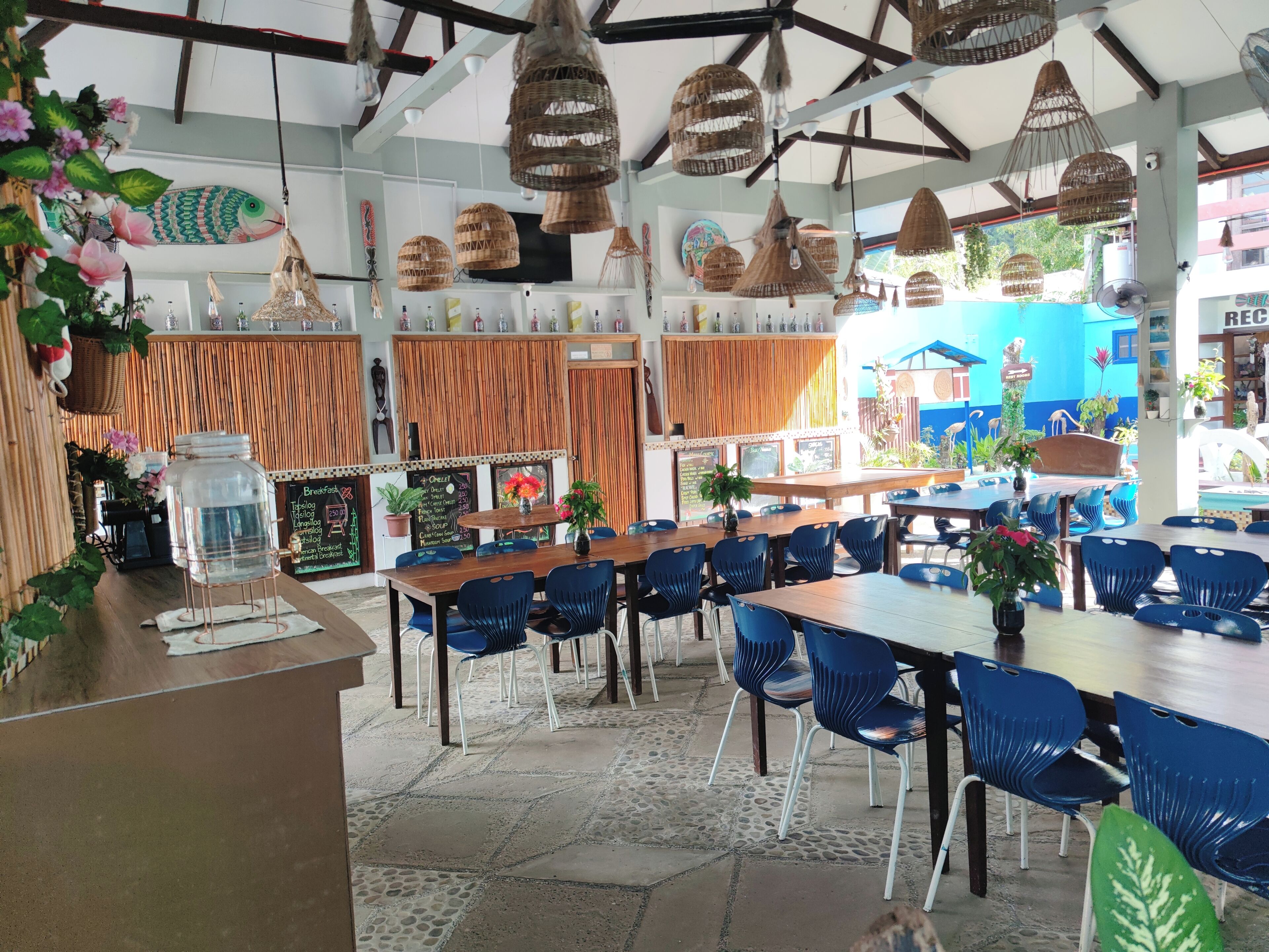 A restaurant with a high ceiling, hanging wicker lamps, and a variety of seating options including tables and chairs.