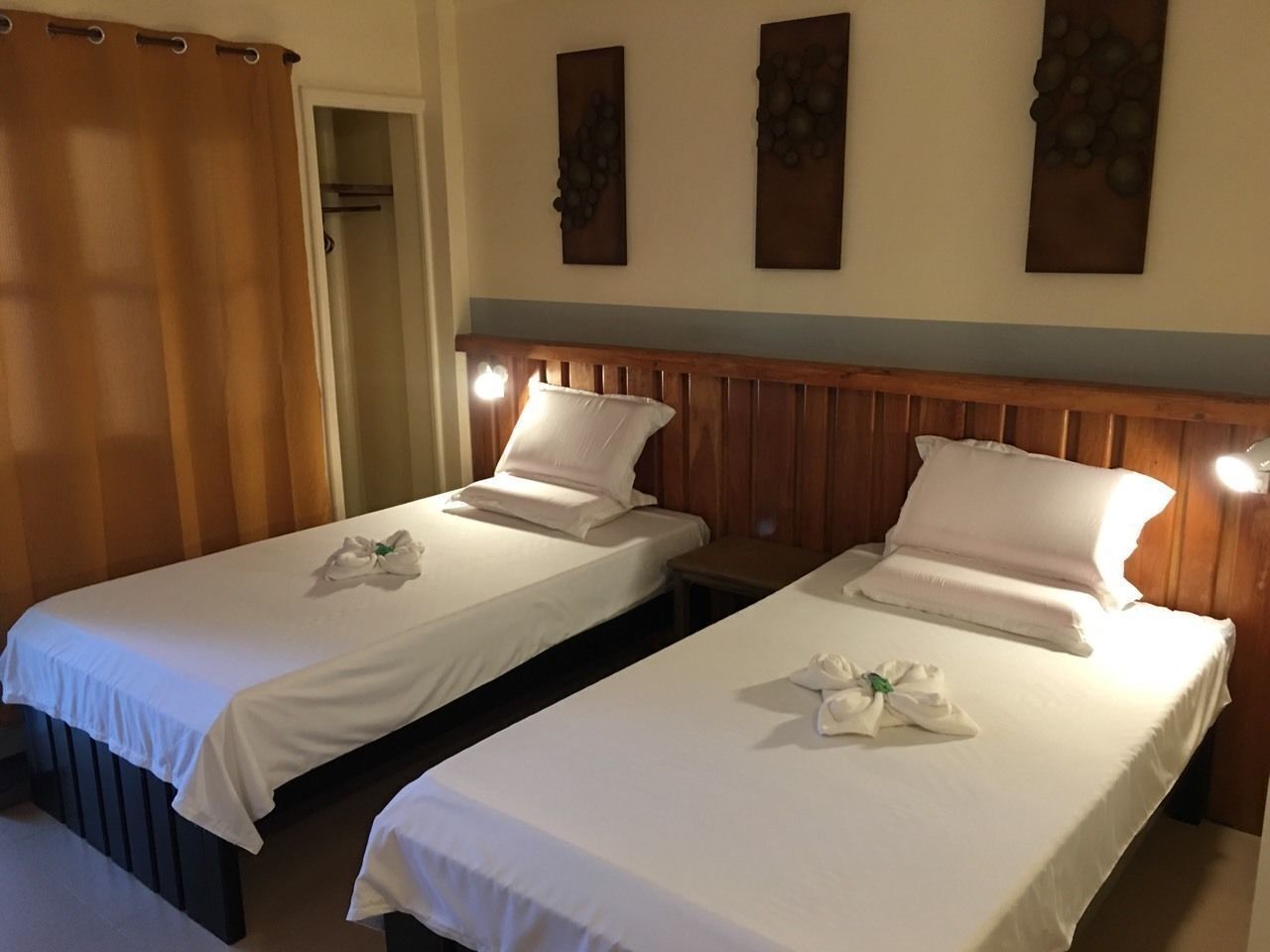 Two single beds with white linens, wooden headboards, and a wooden wall panel.