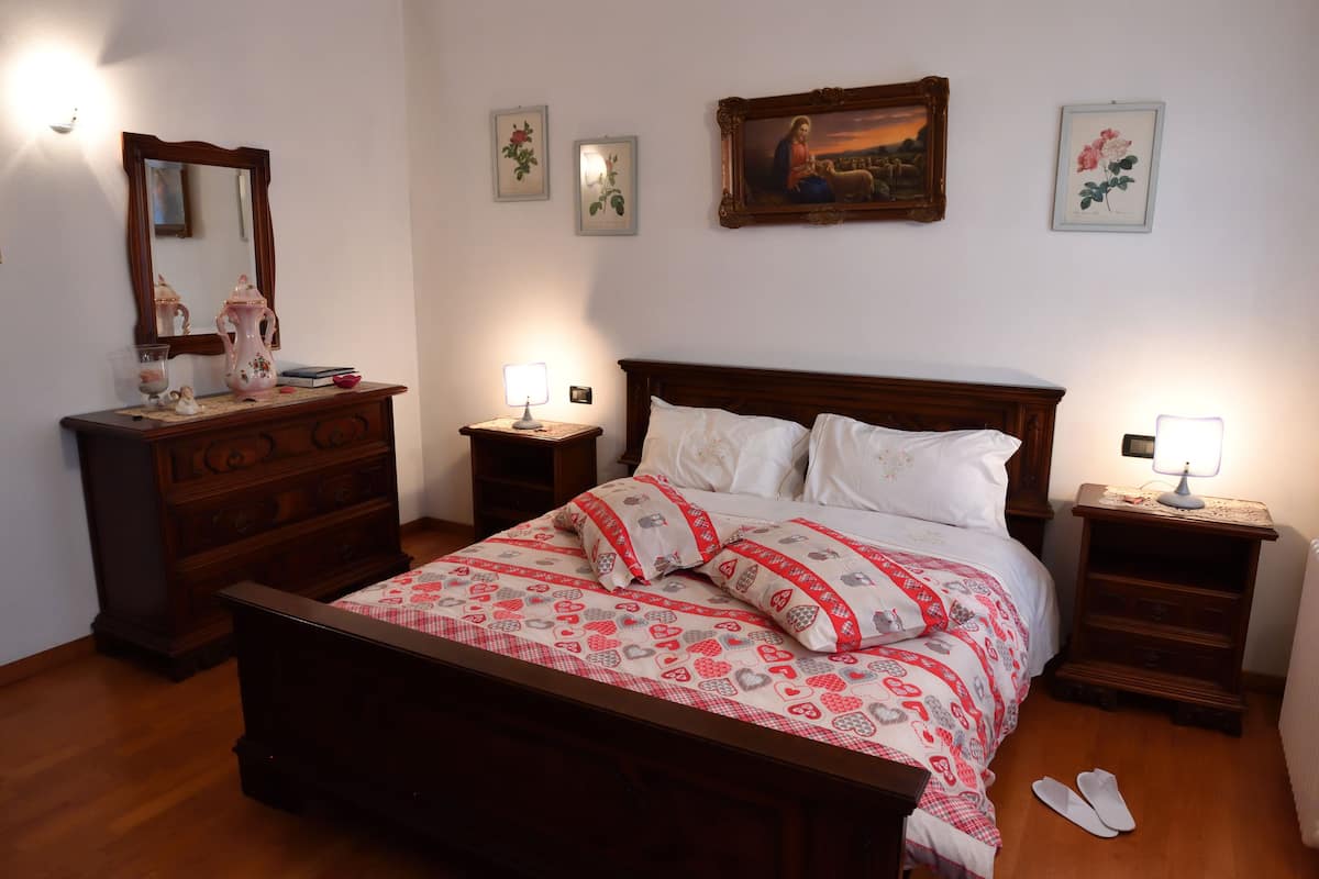 Ein Schlafzimmer mit einem Holzbett, weißer Bettwäsche, einem Schminktisch, einem Nachttisch mit Lampe und einem Spiegel an der Wand.