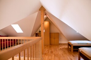 A high-ceilinged attic bedroom with wooden flooring, a wooden staircase, a loft bed, and a skylight.