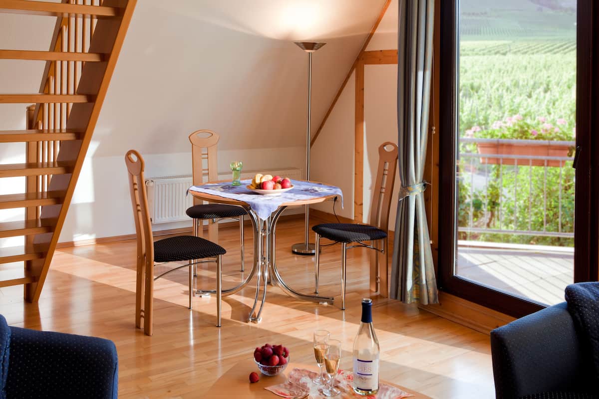 A dining area with a table set for two, a bottle of wine, and a bowl of fruit. A wooden staircase is visible in the background.