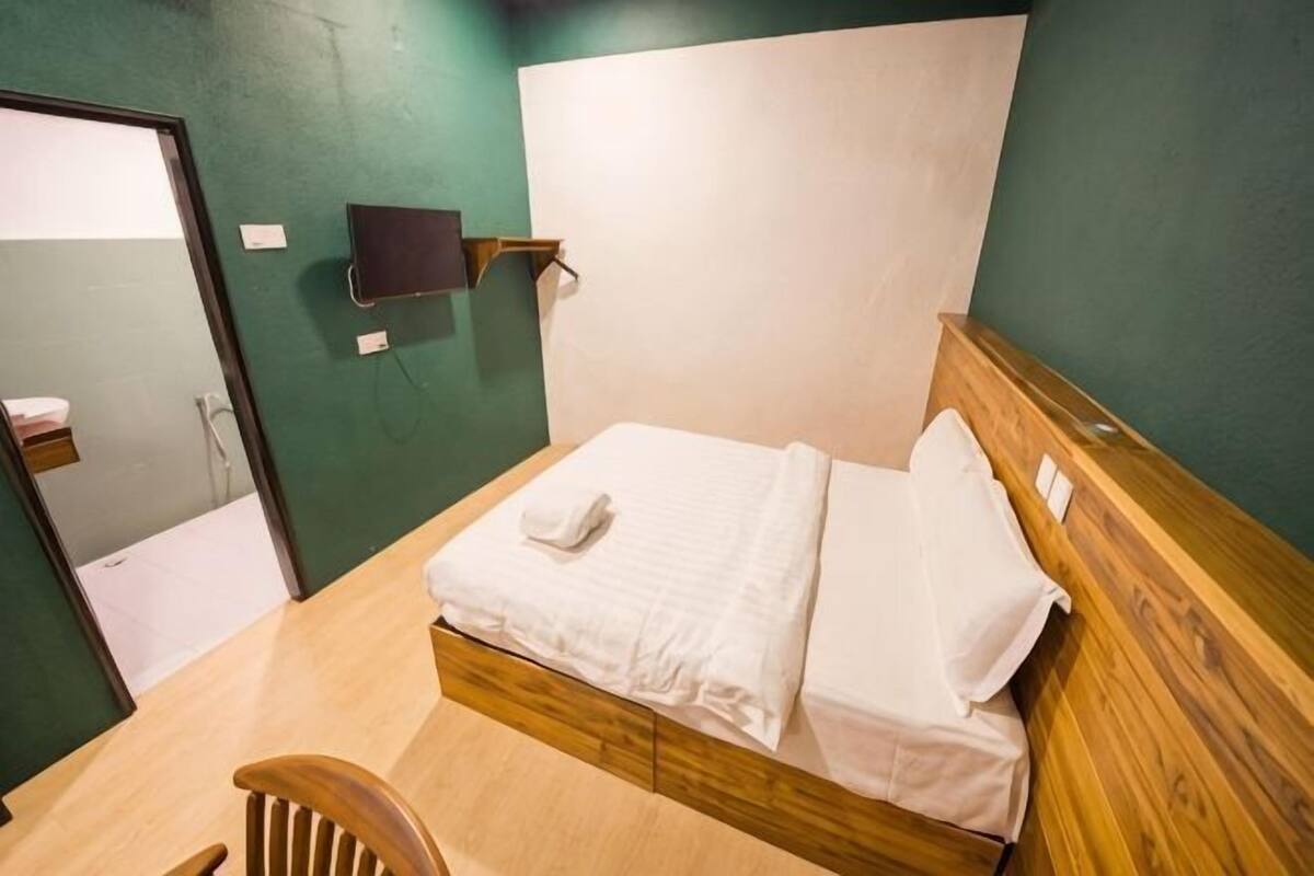 A single bed with a wooden headboard, a small bedside table, and a wall-mounted TV.