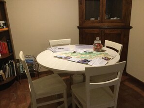 A round dining table with a map and papers, surrounded by white chairs. A wooden cabinet with glass doors is in the background. - Agriturismo Crodi (Miane)