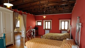 A bedroom with two beds, wooden floors, a red wall, and a ceiling with exposed beams. - Agriturismo Crodi (Miane)
