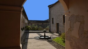 A courtyard with a fountain, a stone pathway, and a building with an arched entrance. - Agriturismo Crodi (Miane)
