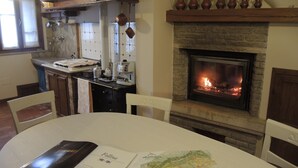 A dining area with a fireplace, a kitchen with hanging pots, and a table with a menu and a map. - Agriturismo Crodi (Miane)