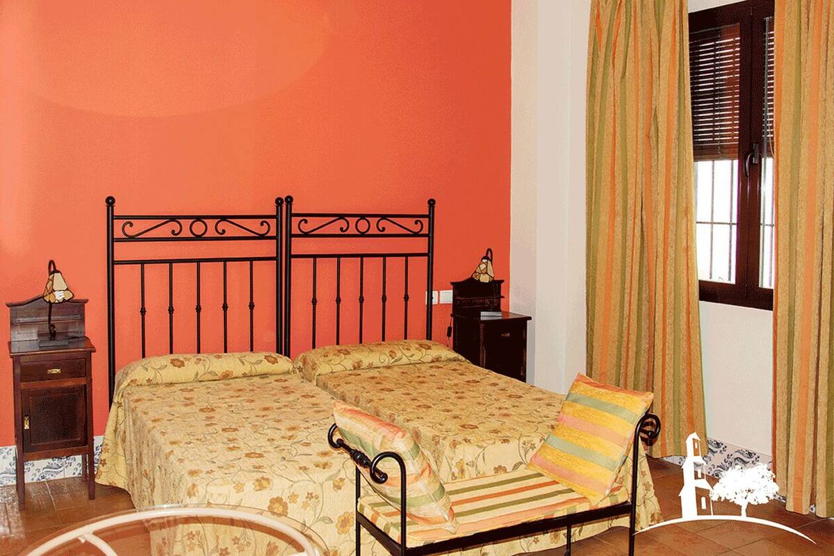 Ein Zimmer mit einem Bett, einem Nachttisch, einer Lampe und Vorhängen.