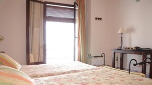 Une chambre avec deux lits, une fenêtre avec des rideaux, une table de chevet avec une lampe et un radiateur.