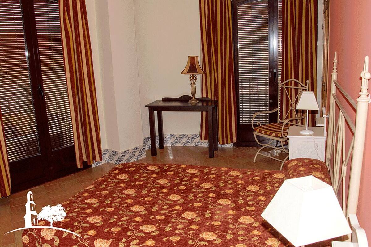 Ein Hotelzimmer mit einem großen Bett, einem Nachttisch mit Lampe, einem Sessel und einem Fenster mit Jalousien.