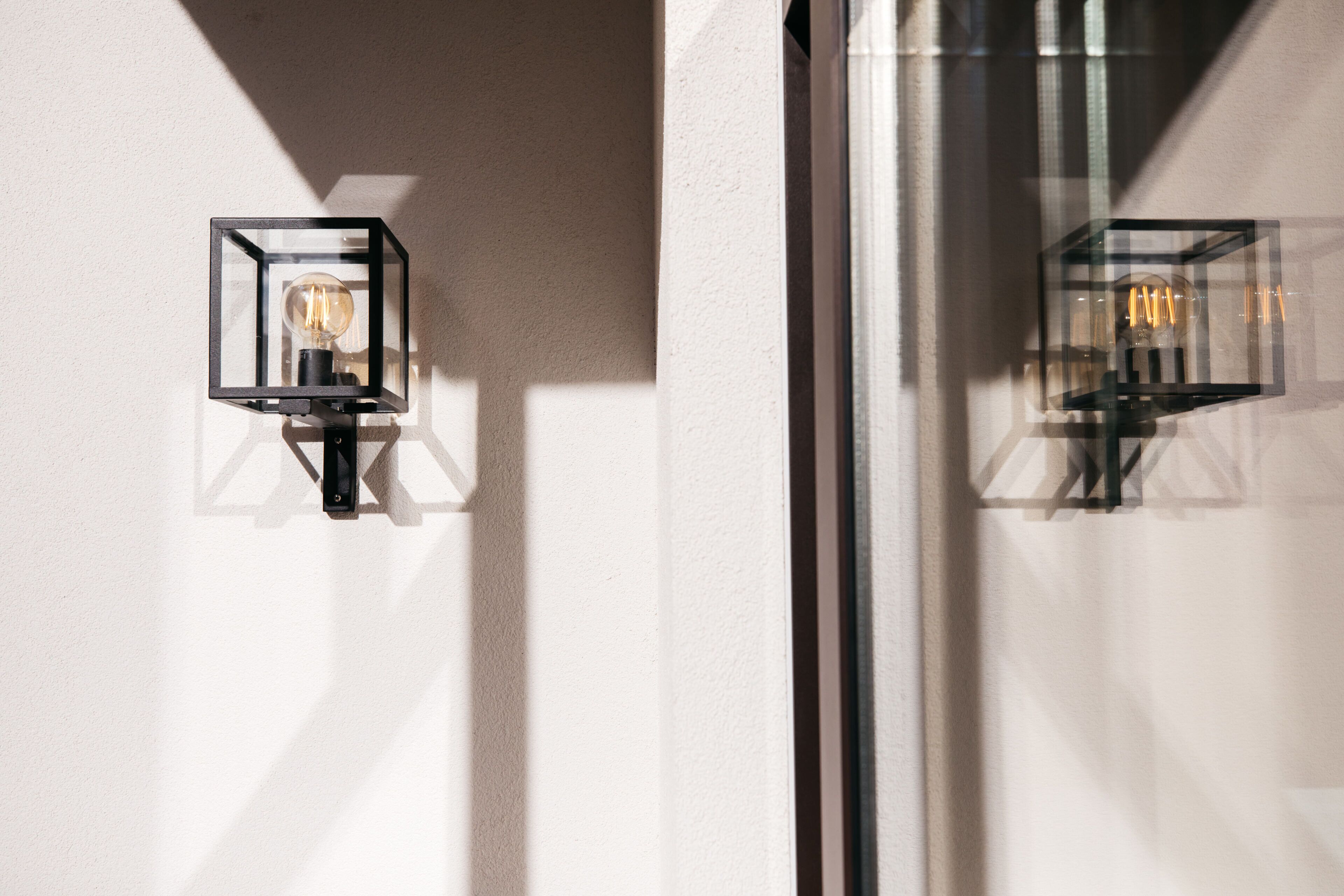 Twee wandlampen met blootliggende lampen, geplaatst tegen een effen muur.