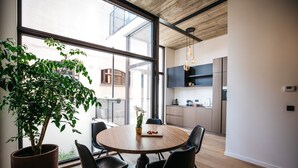 Un comedor moderno con una mesa redonda, sillas negras, una planta en maceta y vistas a la cocina y al balcón.