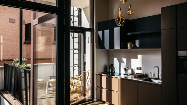 Una cocina moderna con un ventanal grande, un comedor con sillas de mimbre y vista a un edificio de ladrillo.