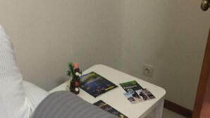 Un sofá blanco con una manta gris, una mesita auxiliar blanca con revistas y una planta pequeña, además de una puerta de madera.