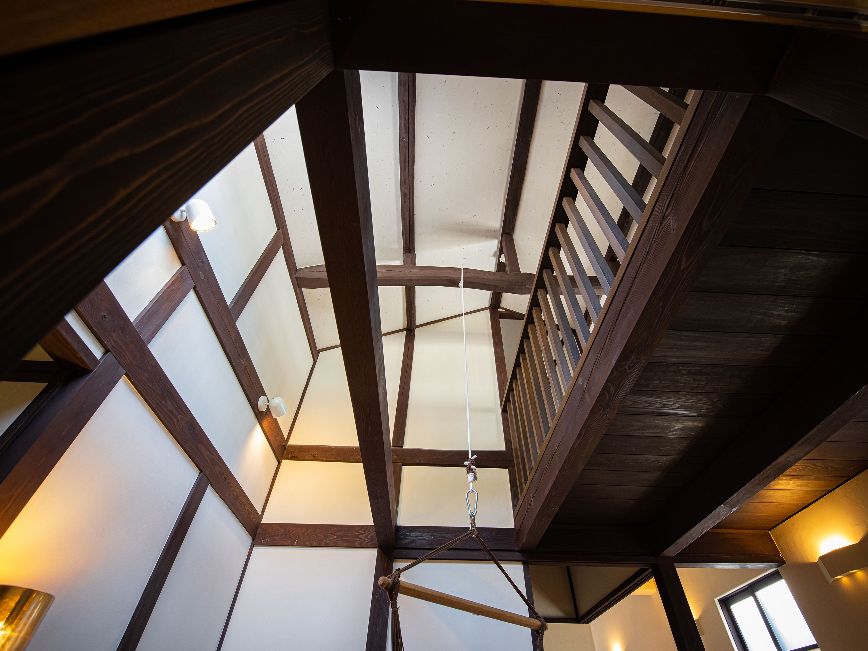 A room with a sloped ceiling, wooden beams, and a hanging light fixture.