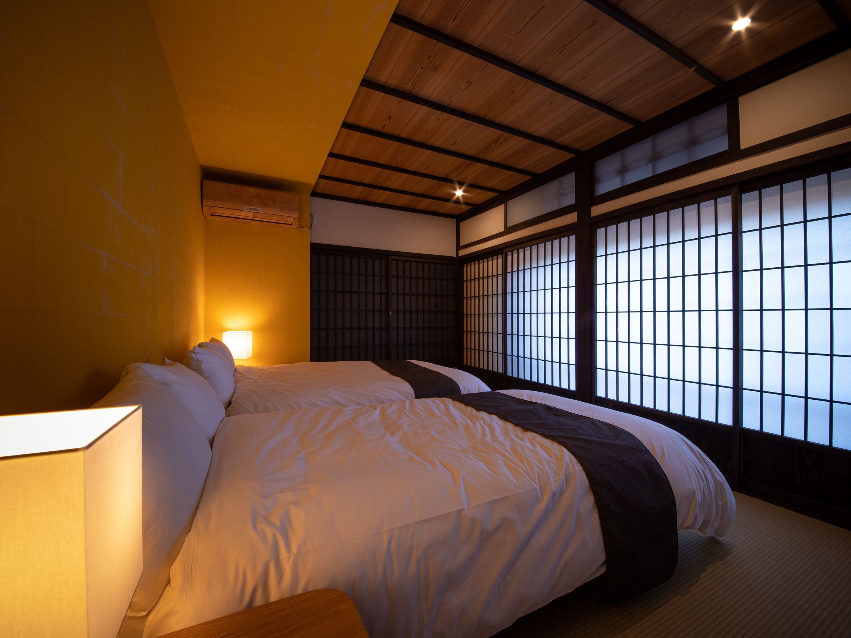 Une pièce de style japonais traditionnel, avec un sol recouvert de tatamis, un plafond bas avec des poutres en bois et des panneaux coulissants en papier.
