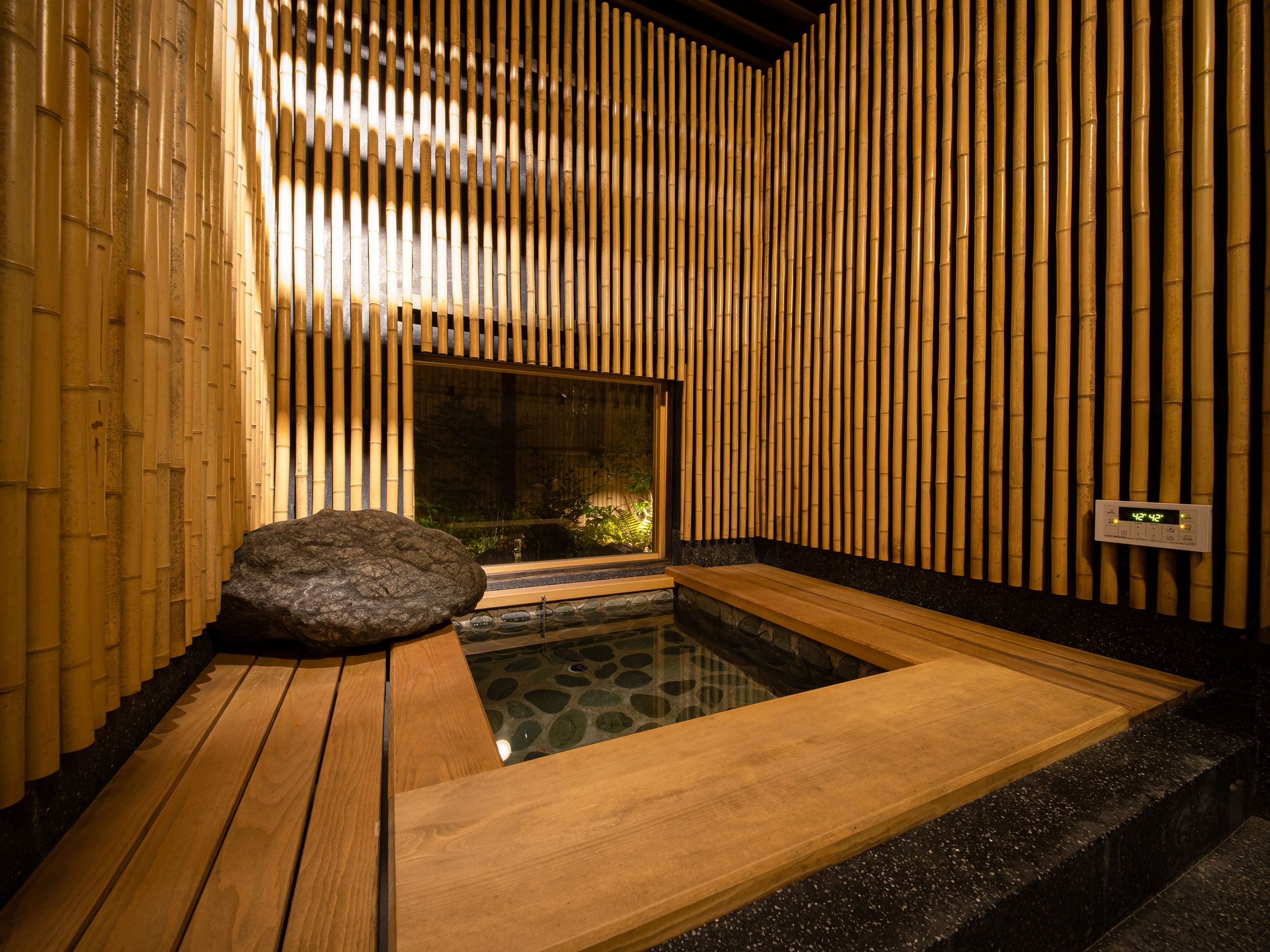 Un onsen japonais traditionnel, avec un sol en bois, un bassin en pierre et des murs en bambou.