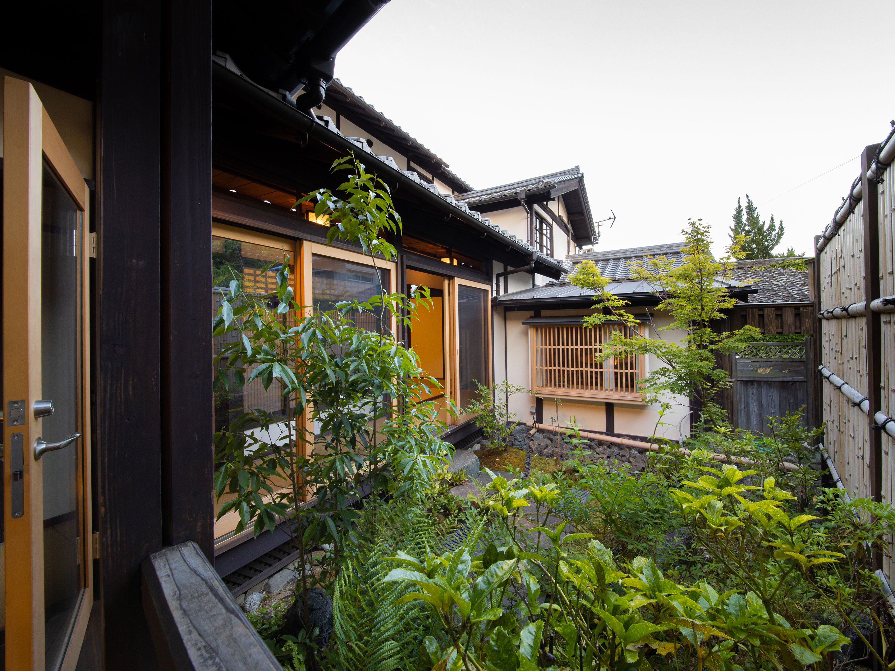 Una casa tradicional japonesa con fachada de madera, un puertas correderas y un pequeño jardín con diversas plantas.