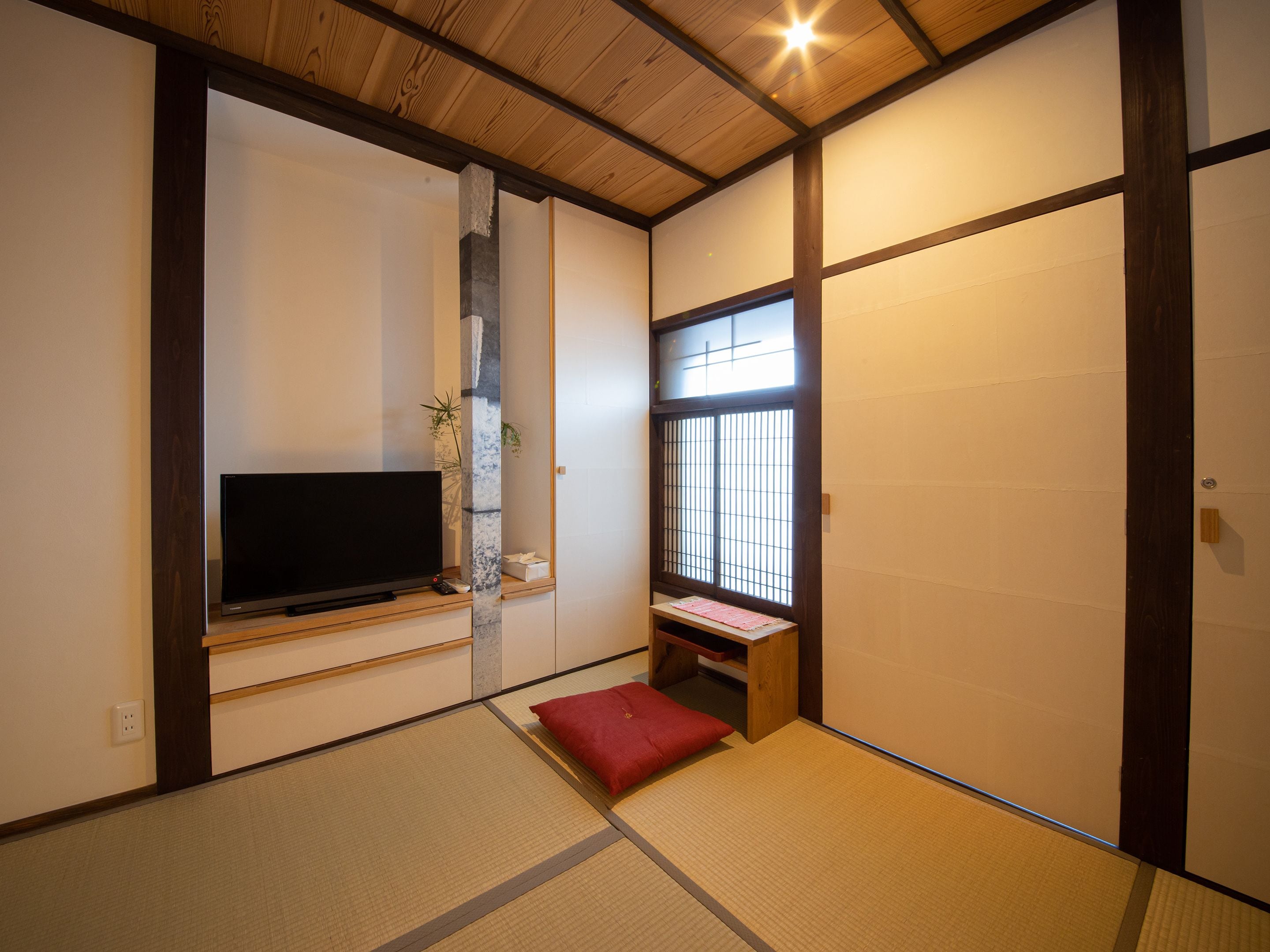 Una habitación japonesa tradicional con suelo de tatami, televisión, puerta corredera y ventana con diseño de cuadrícula.