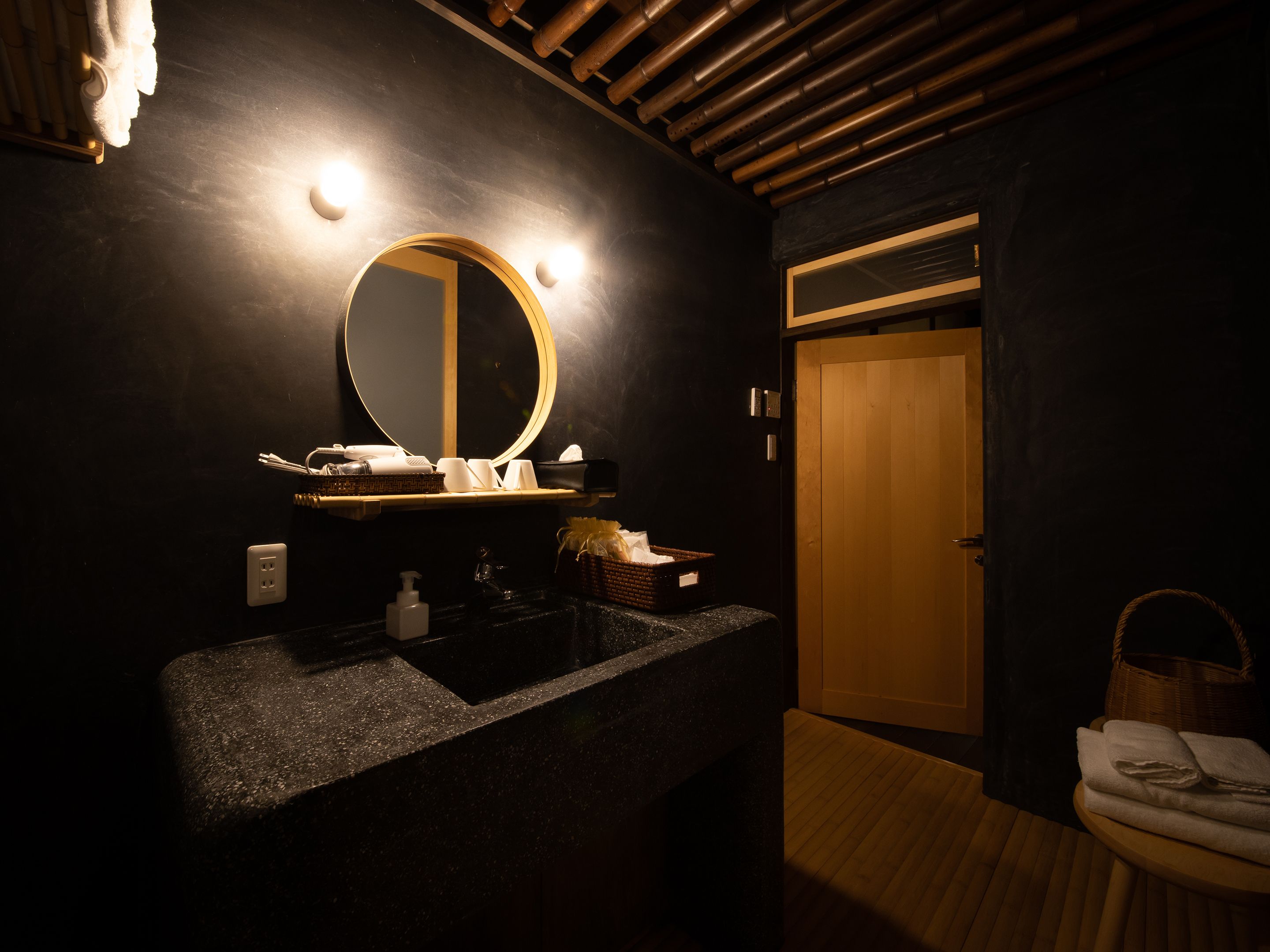 A modern bathroom with a granite sink, a round mirror, and a wooden door.
