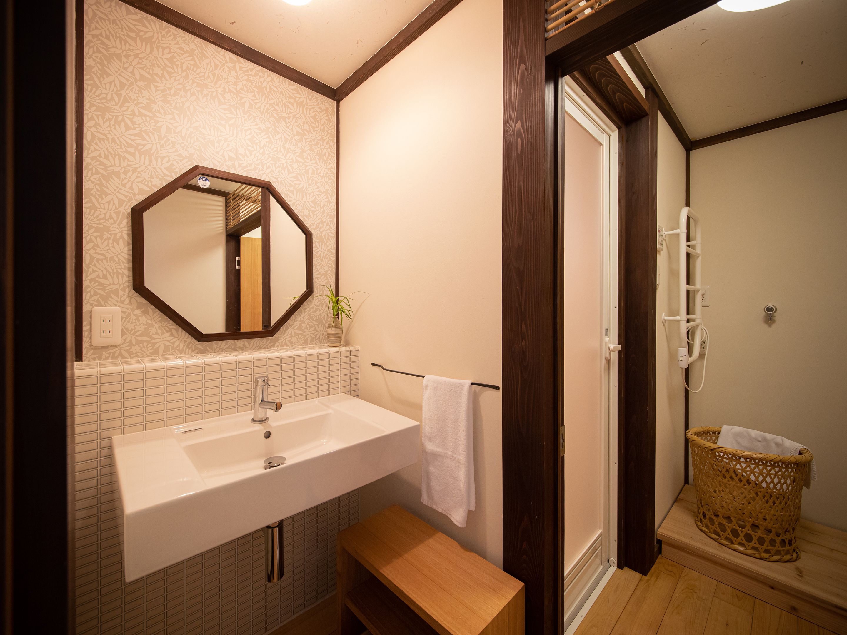 A bathroom with a white sink, a wooden bench, a mirror, and a shower area.