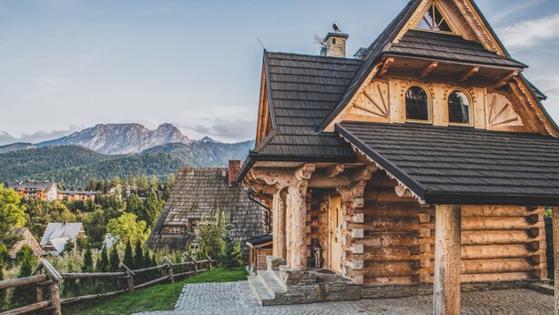A log cabin with a stone foundation, wooden beams, and a steeply pitched roof.