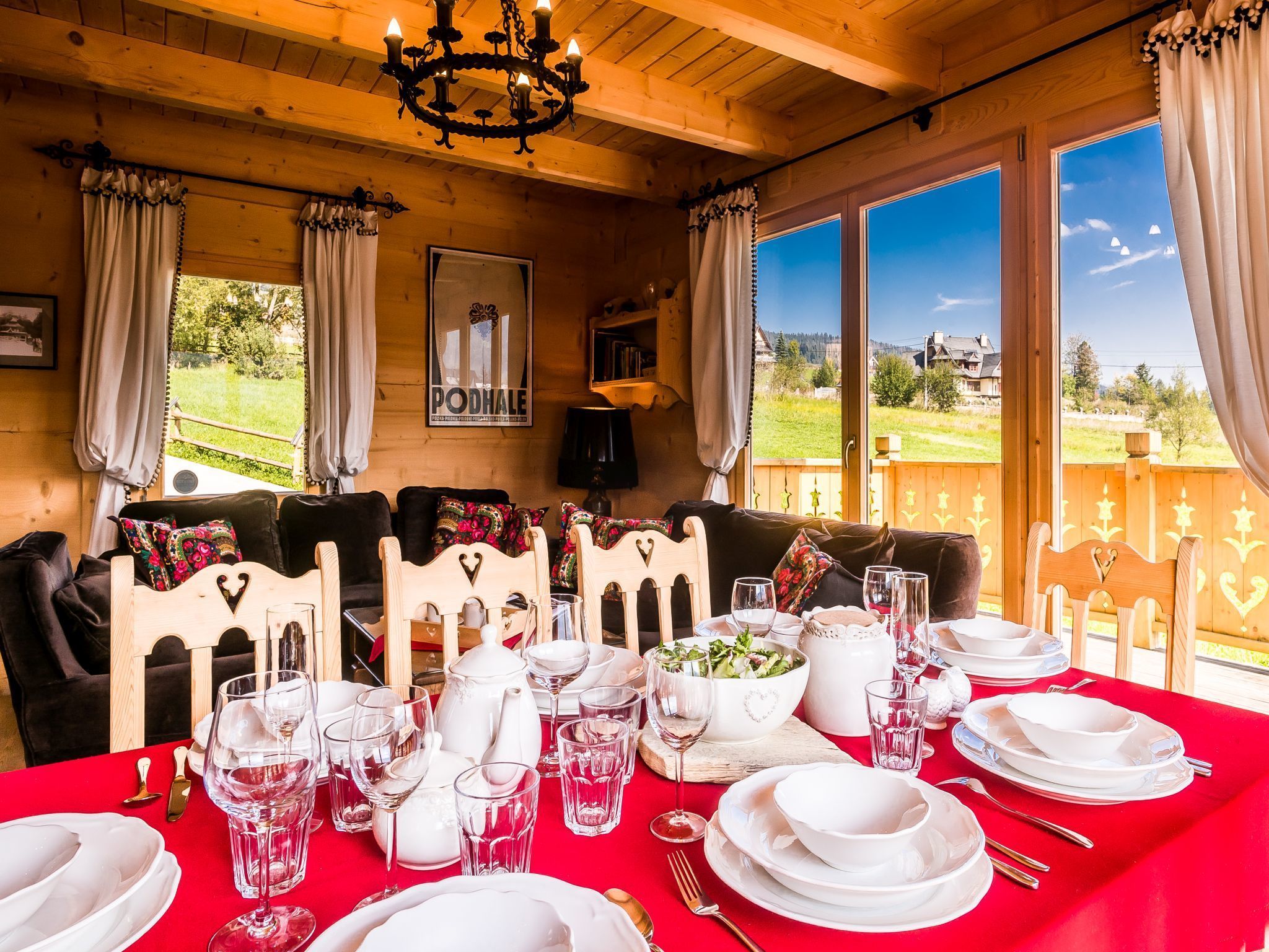 Un coin repas avec une table rouge dressée pour le repas, des meubles en bois et une vue sur l’extérieur.