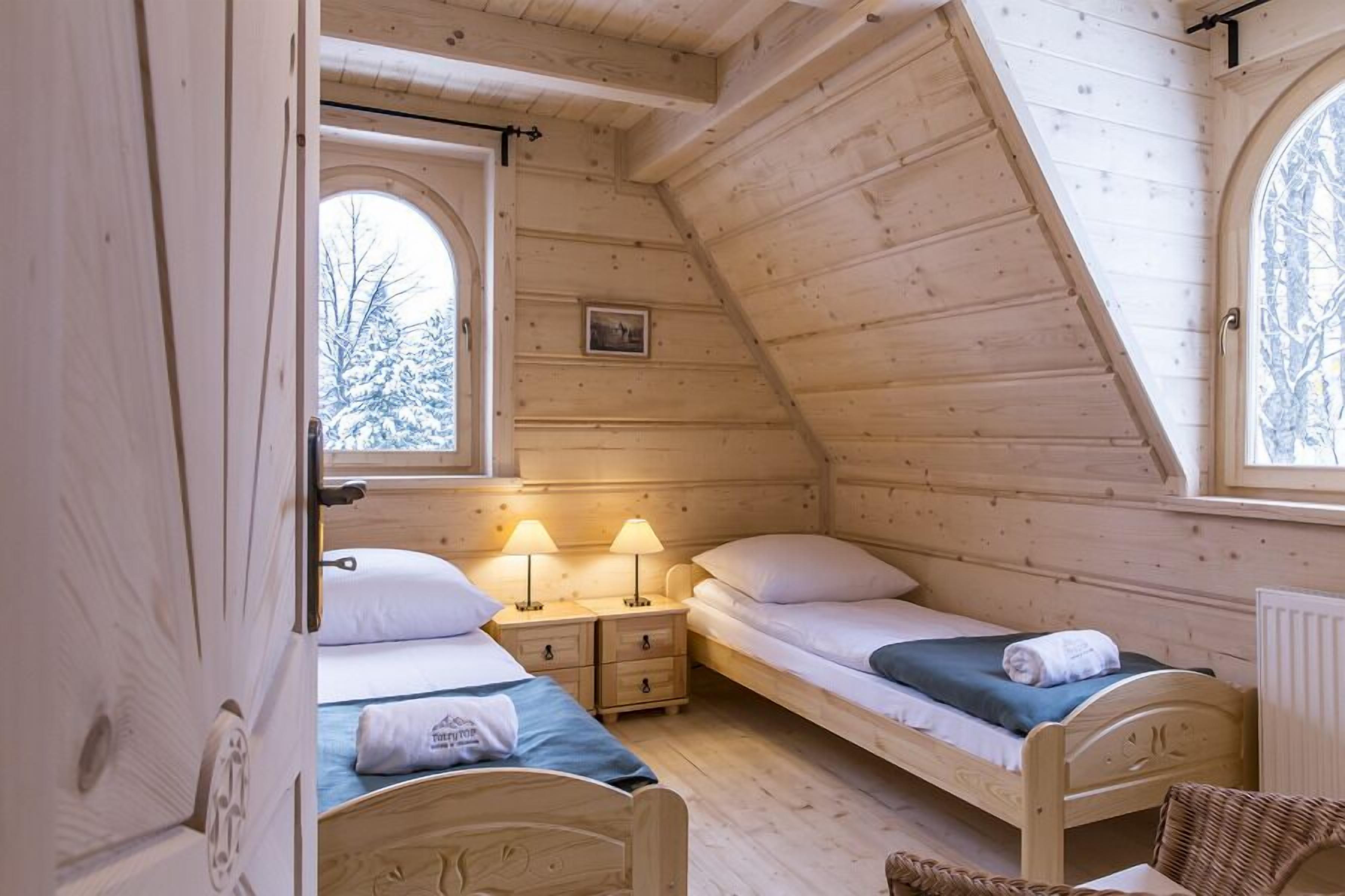Une chambre confortable, aménagée dans un chalet en bois, avec deux lits simples, une petite fenêtre et un tableau au mur.