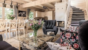 A wooden interior with a dining area, a black armchair, a glass coffee table, and a staircase.