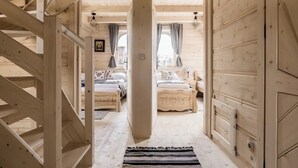A wooden interior with a staircase, a bed, a sofa, and a window with curtains.