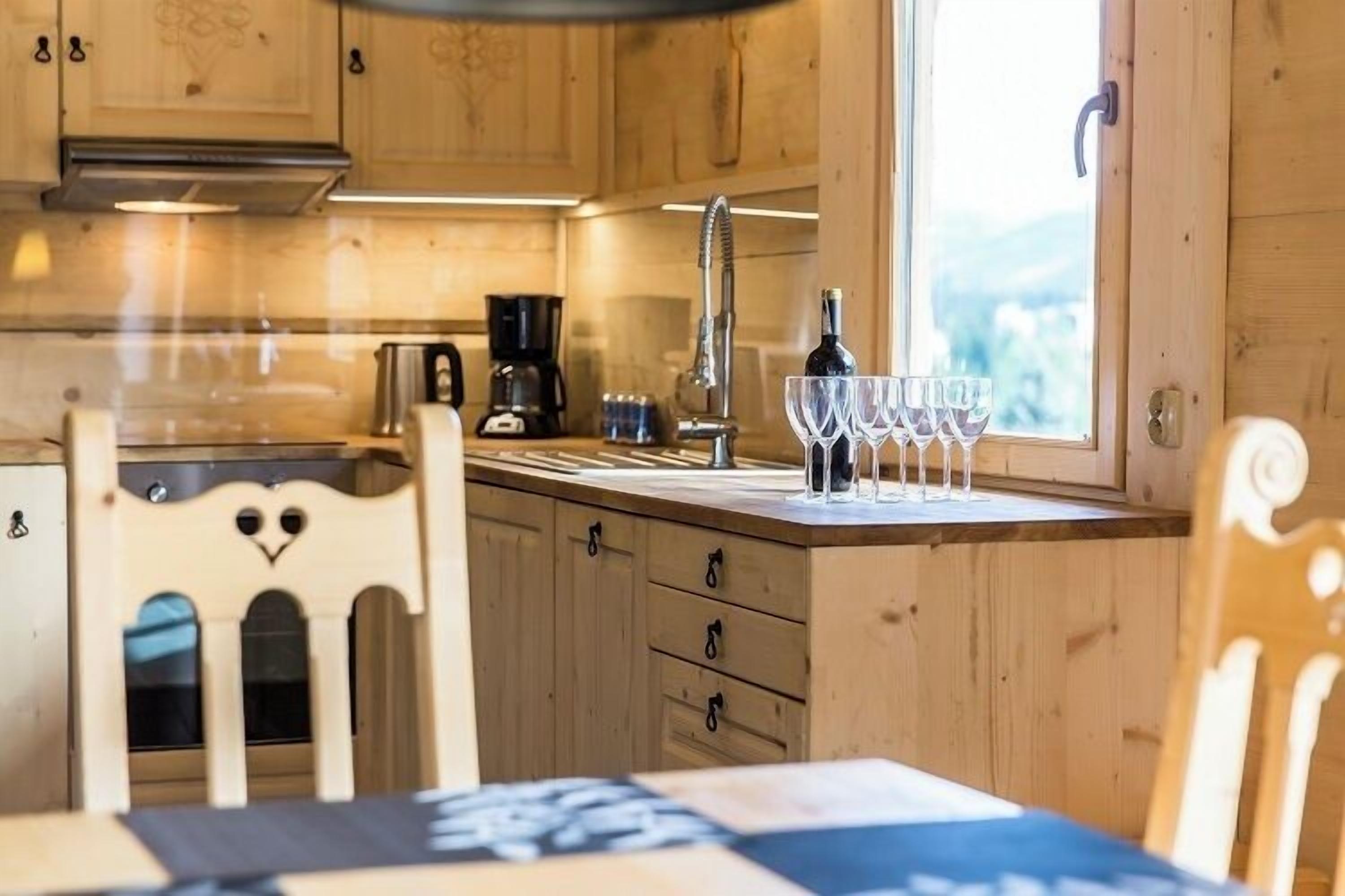 A wooden kitchen with a window, a sink, cabinets, and a dining table with chairs.