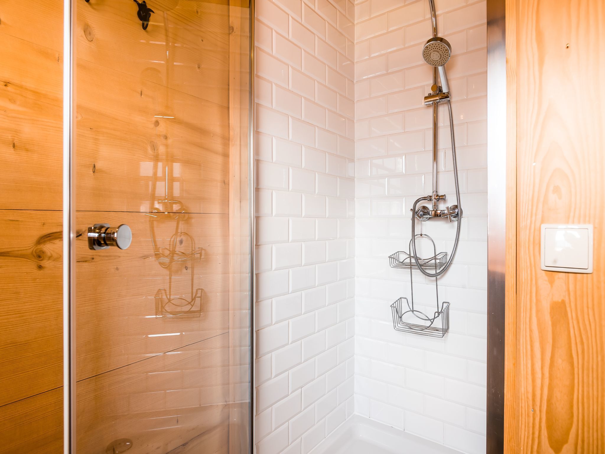 Une salle de bain moderne avec une douche à parois de verre, des murs recouverts de carreaux blancs et une porte en bois.