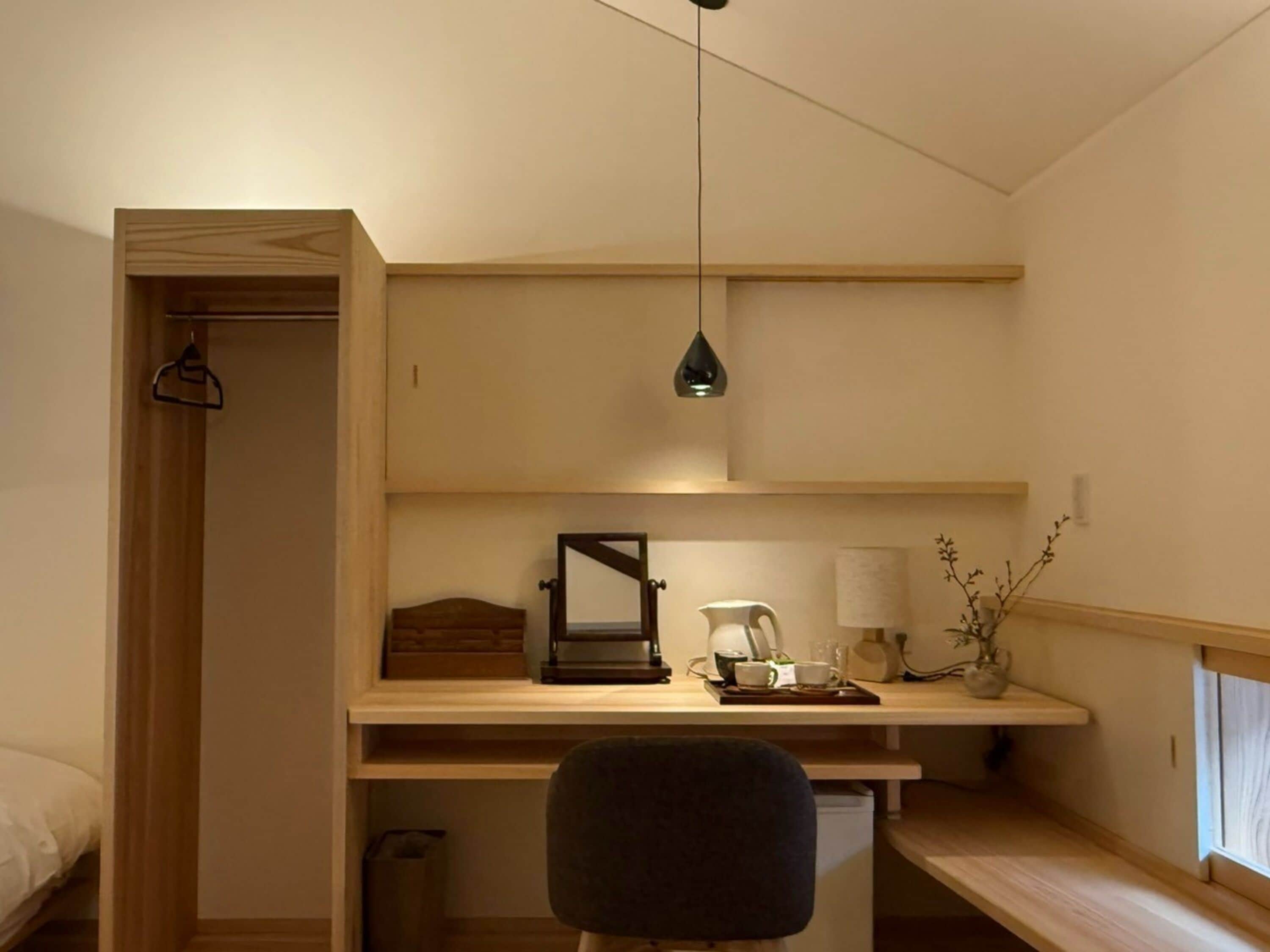 A bedroom with a bed, a desk with a chair, a hanging light, and a window.