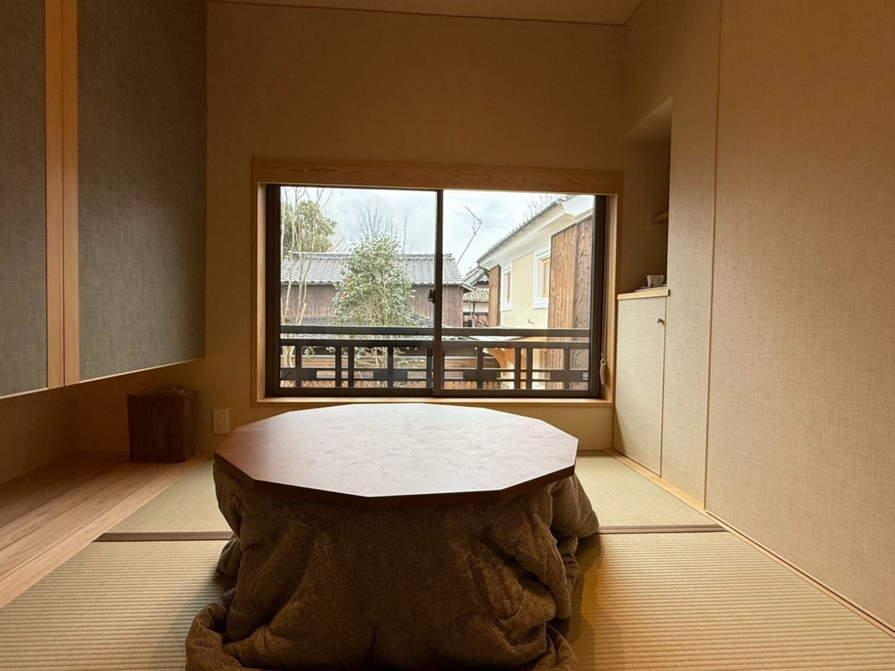 A tatami mat room with a tatami mat table, a sliding door with a view of a traditional building, and a wooden bench outside.