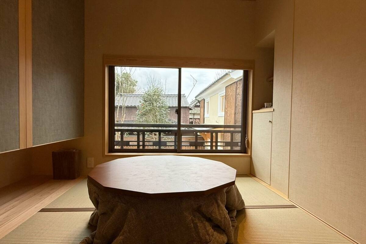 A tatami mat room with a tatami mat table, a sliding door with a view of a traditional building, and a wooden bench outside.